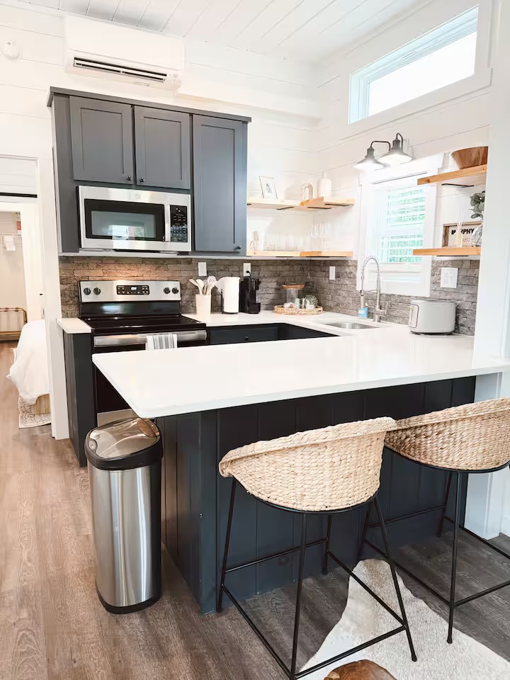 Tiny Timber kitchen with navy cabinets, stainless appliances, and woven bar stools