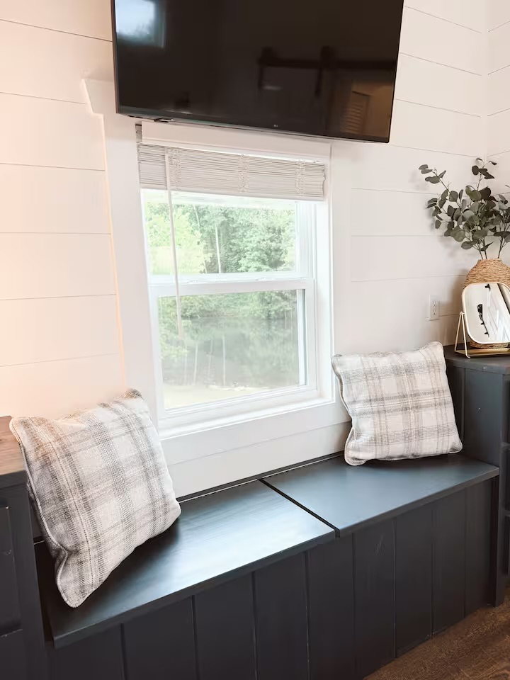 Tiny Timber storage bench under a window with plaid pillows and mounted TV