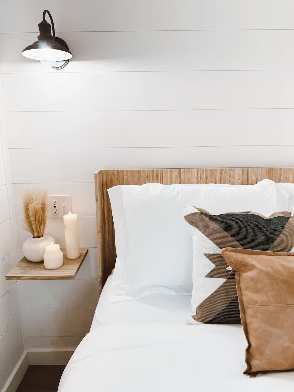 Tiny Timber bedside detail with wood headboard, sconce, and layered pillows